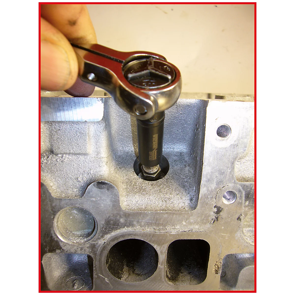 Eine Hand hält eine Ratsche, die eine Schraube in ein Motorenbauteil dreht.